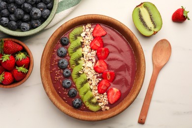 Bowl of delicious smoothie with fresh blueberries, strawberries, kiwi slices and oatmeal on white marble table, flat lay
