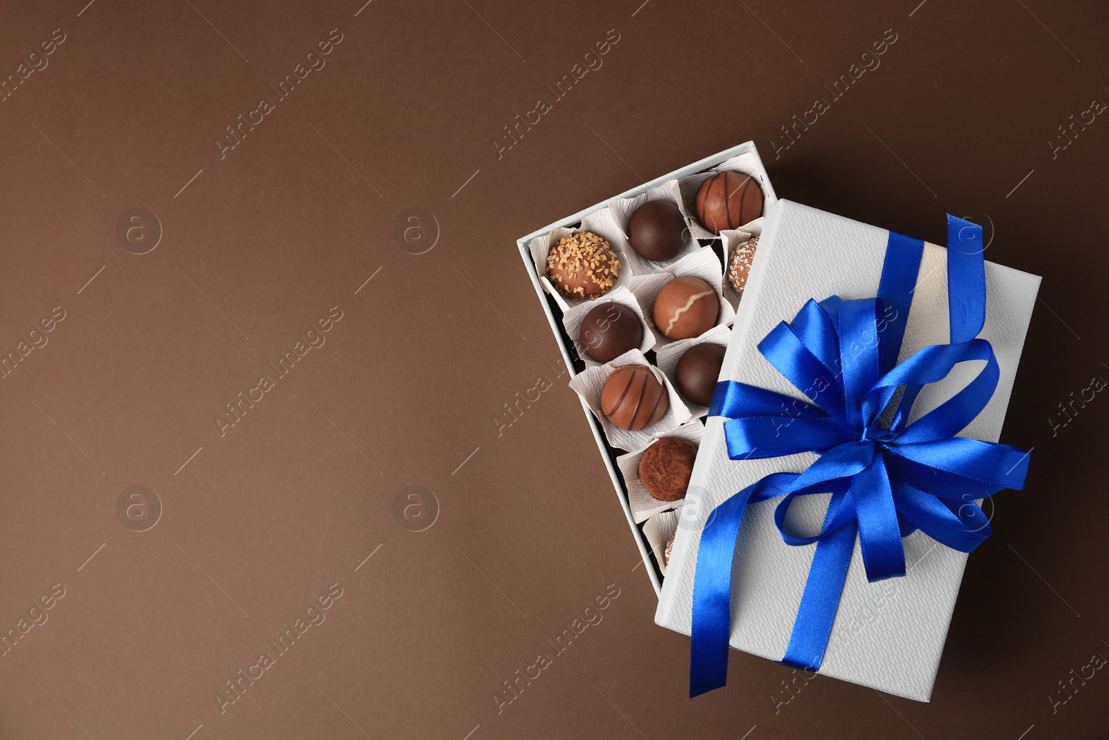 Photo of Box with delicious chocolate candies on brown background, top view. Space for text