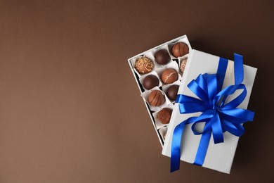 Photo of Box with delicious chocolate candies on brown background, top view. Space for text