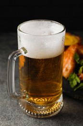 Photo of Mug with delicious beer and baked chicken wings on grey table, closeup