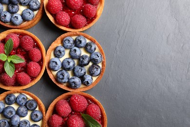 Photo of Tartlets with different fresh berries on black table, flat lay and space for text. Delicious dessert