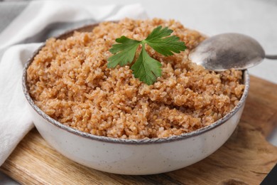 Tasty wheat porridge with parsley in bowl on wooden table, closeup