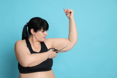 Photo of Obese woman with scissors on light blue background, space for text. Weight loss surgery