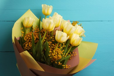 Bouquet with beautiful tulips and mimosa flowers on light blue wooden table, top view