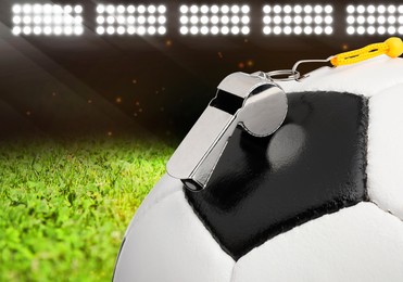 Image of Referee equipment. Soccer ball and whistle on green football field under stadium lights, closeup
