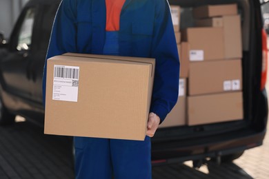 Photo of Courier with parcel near delivery van outdoors, closeup. Space for text