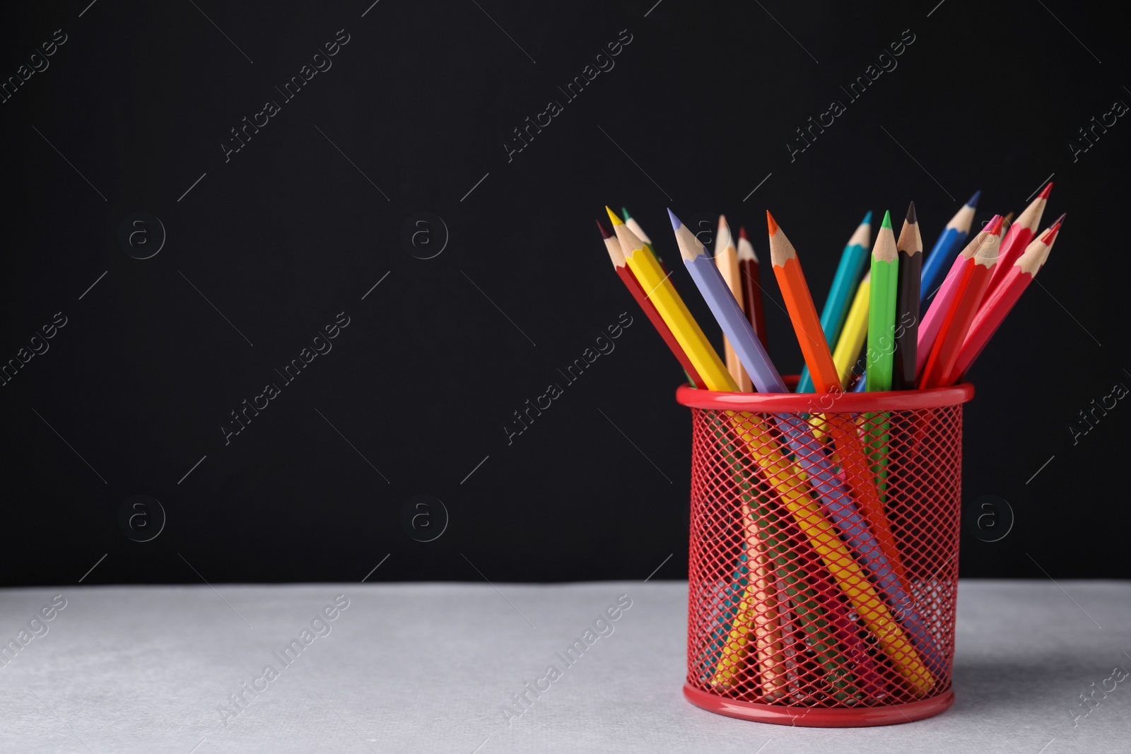 Photo of Many colorful pencils in holder on light table against black background, space for text