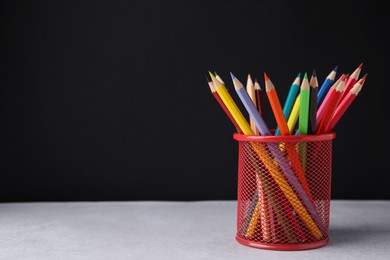 Many colorful pencils in holder on light table against black background, space for text