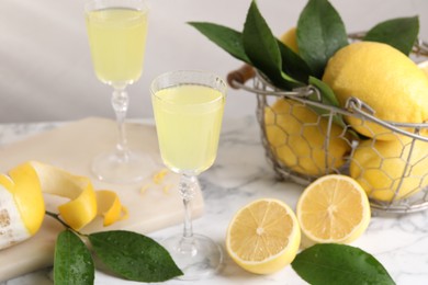 Photo of Tasty limoncello liqueur, lemons and green leaves on white marble table