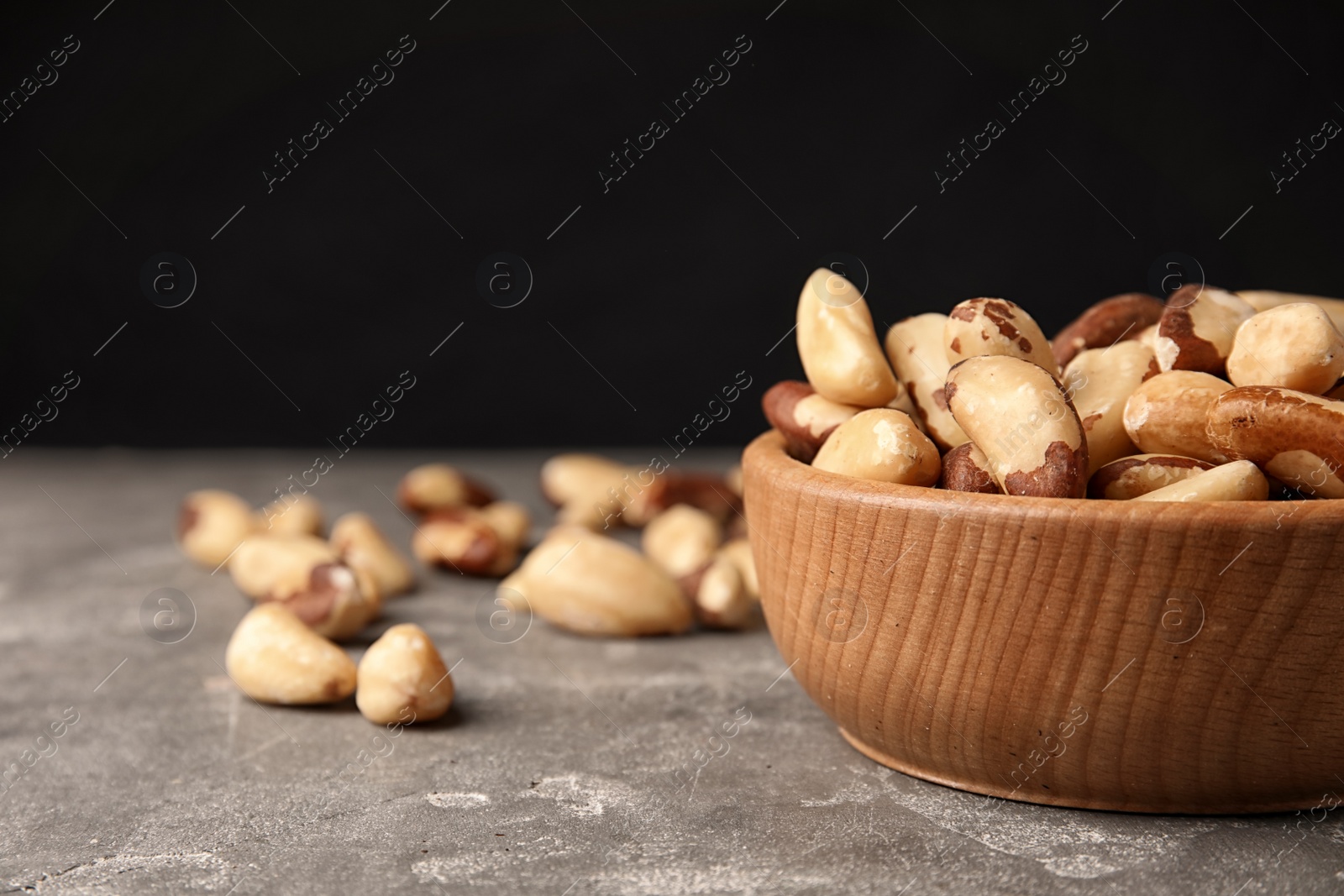 Photo of Bowl with tasty Brazil nuts on grey table. Space for text