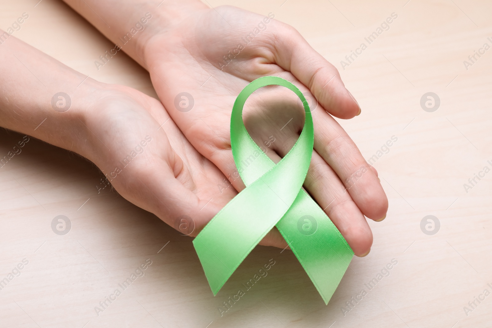 Photo of World Mental Health Day. Woman holding green ribbon on wooden background, closeup