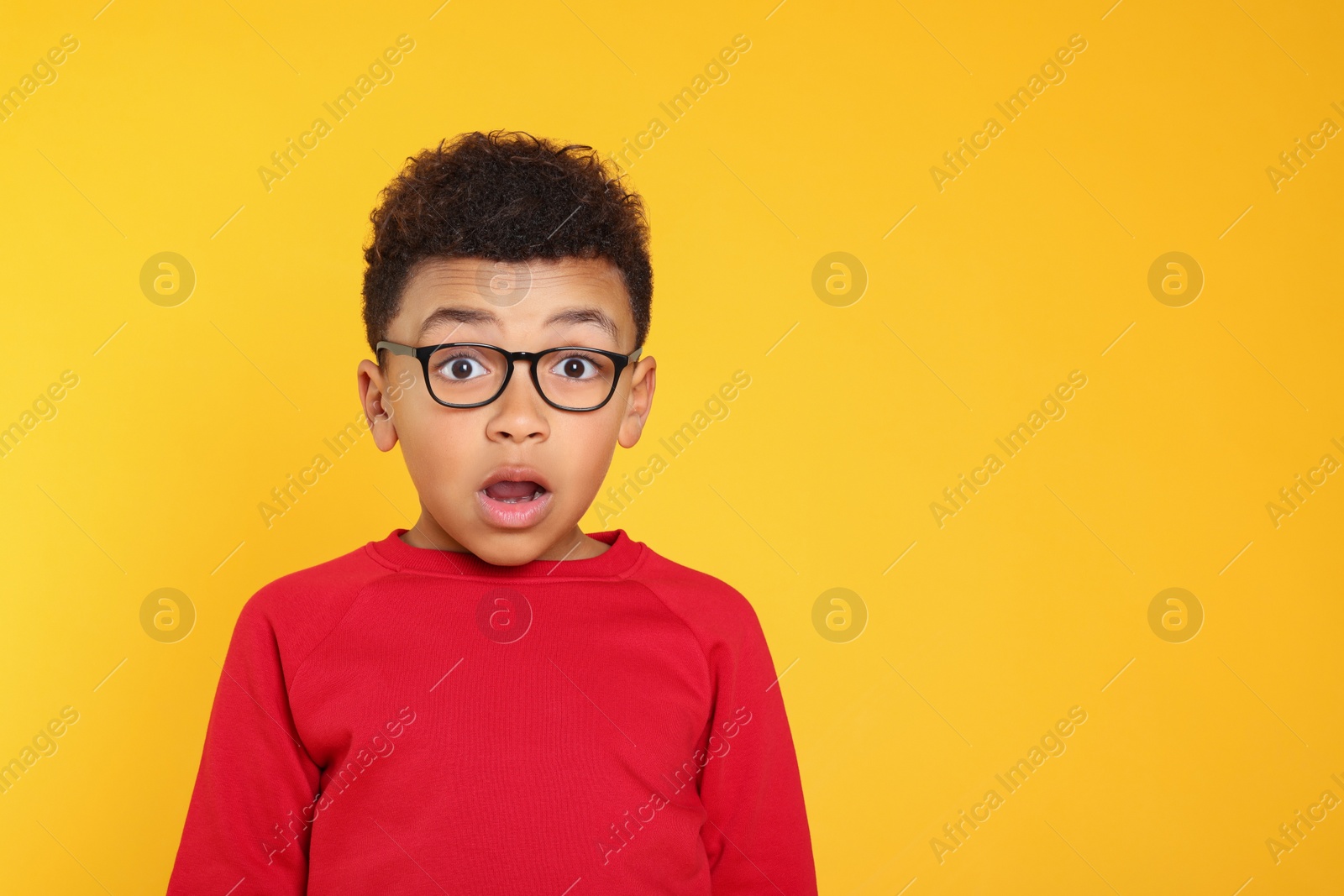 Photo of Emotional African-American boy with glasses on yellow background. Space for text