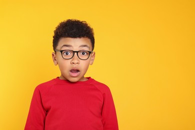 Emotional African-American boy with glasses on yellow background. Space for text