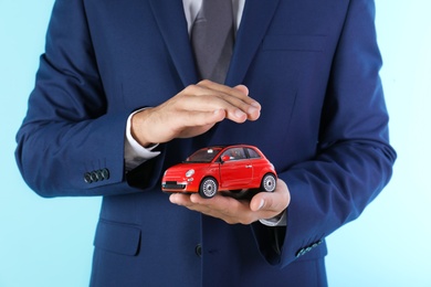 Insurance agent holding toy car on color background, closeup