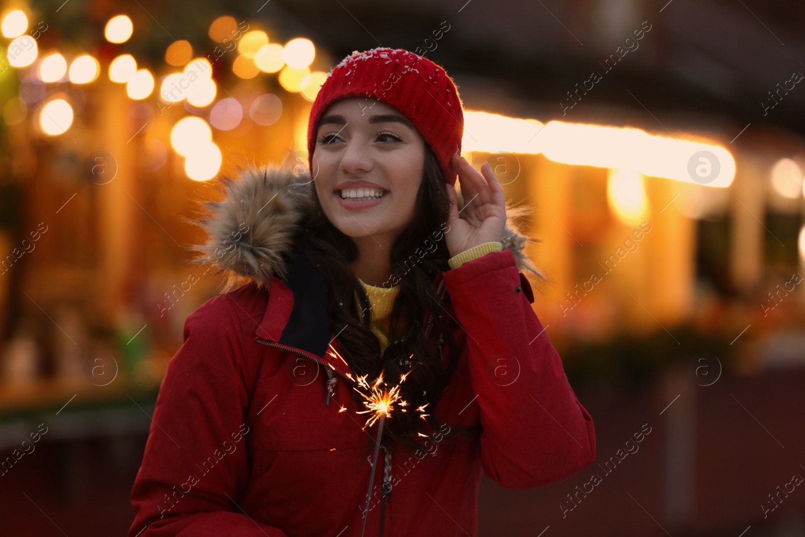 Photo of Happy young woman with sparkler at winter fair in evening. Christmas celebration