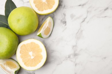 Photo of Whole and cut sweetie fruits with green leaves on white marble table, flat lay. Space for text