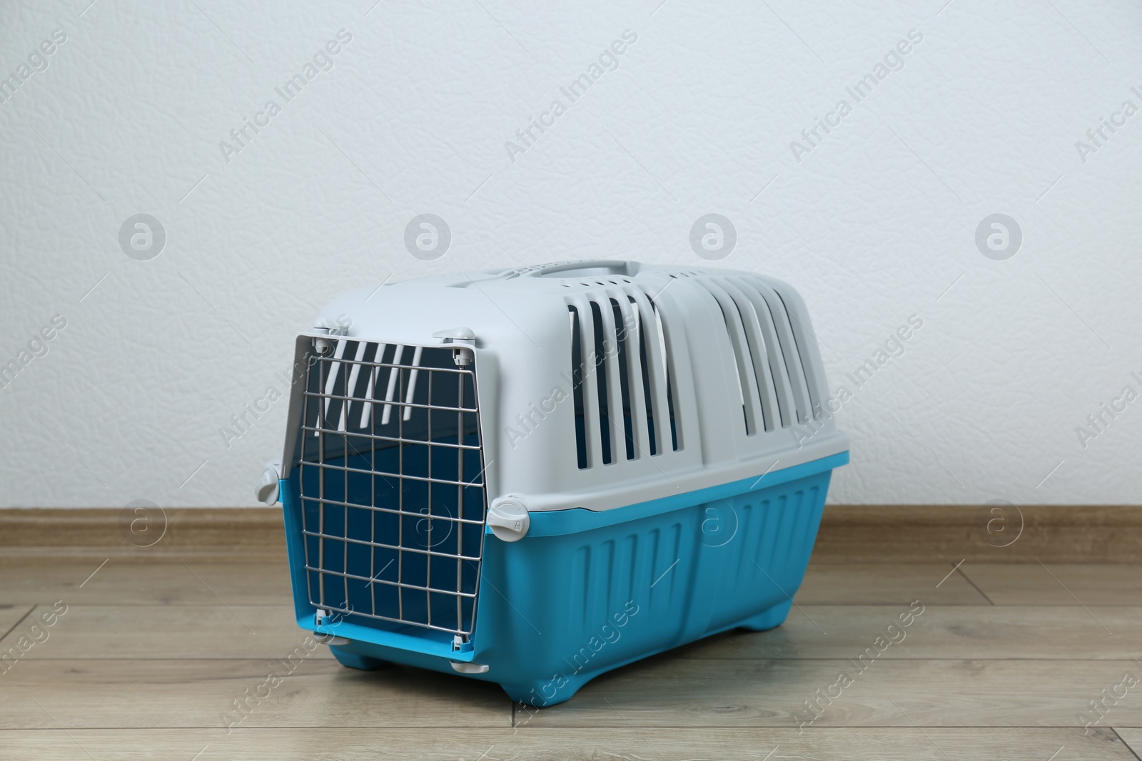 Photo of Light blue pet carrier on floor near white wall