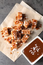 Tasty candies, caramel sauce and salt on grey table, top view