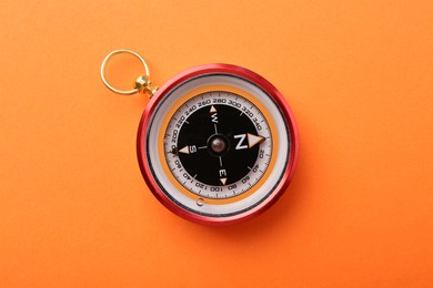 Photo of Compass on orange background, top view. Navigation equipment