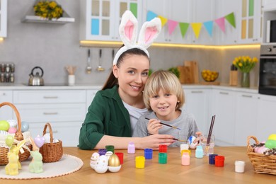 Photo of Mother and her son painting Easter eggs at table in kitchen