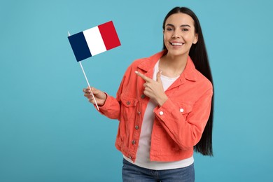 Happy young woman pointing at flag of France on light blue background