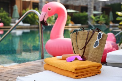 Photo of Beach accessories on sun lounger and float in shape of flamingo near outdoor swimming pool. Luxury resort