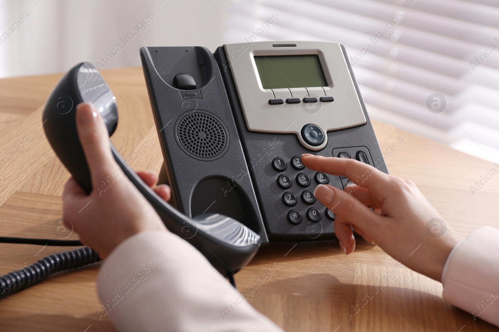 Photo of Woman using desktop telephone at wooden table in office, closeup. Hotline service