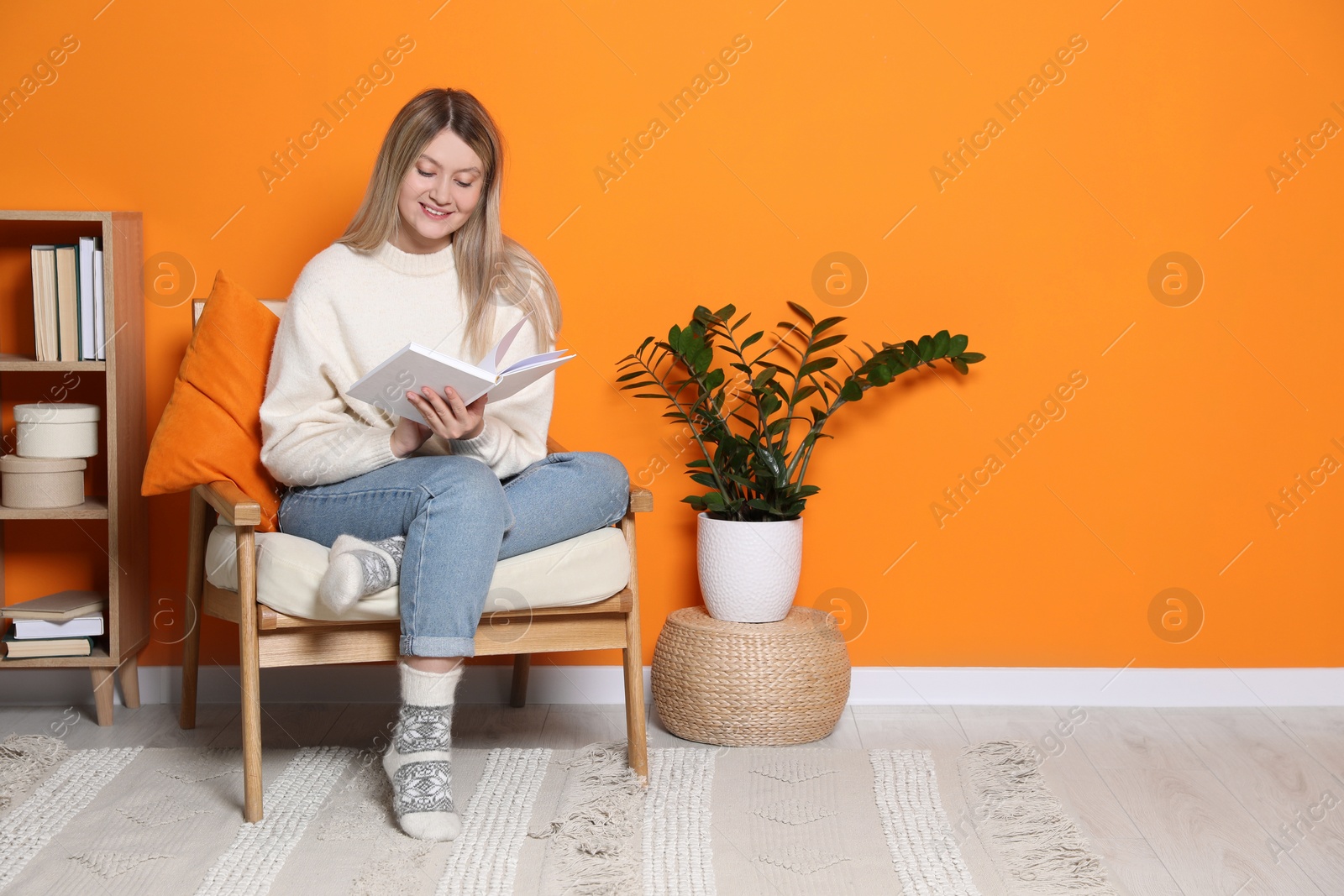 Photo of Young woman reading book in armchair at home, space for text. Interior design