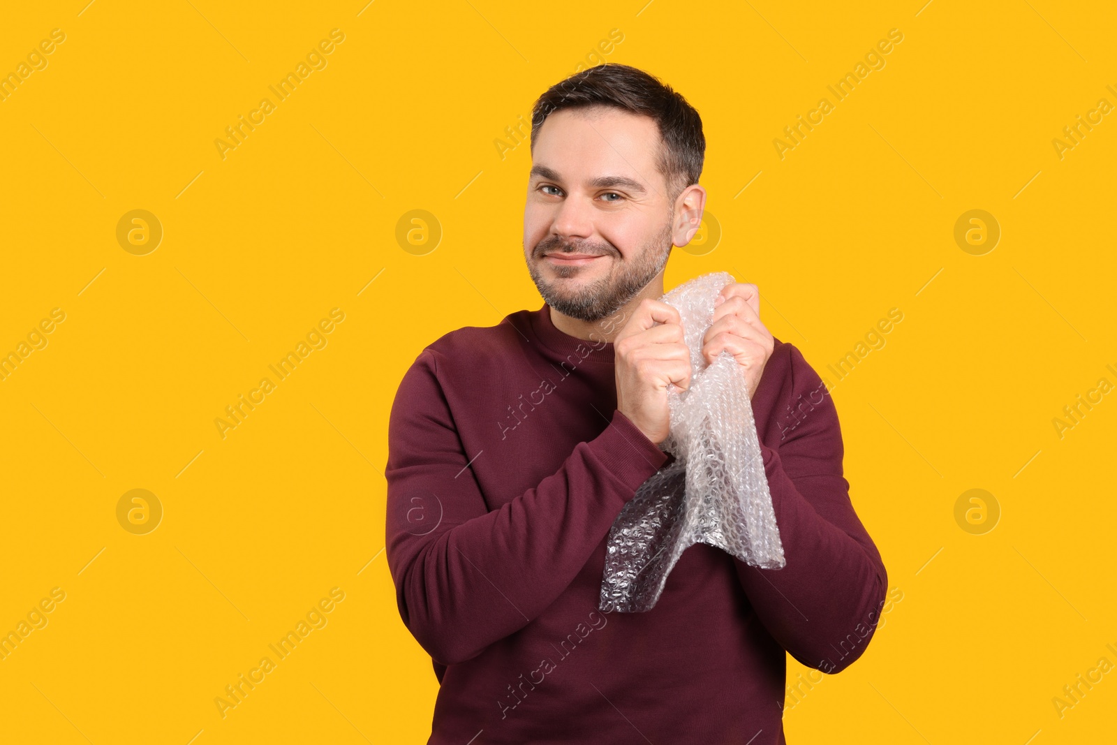 Photo of Happy asian man with bubble wrap on orange background. Space for text