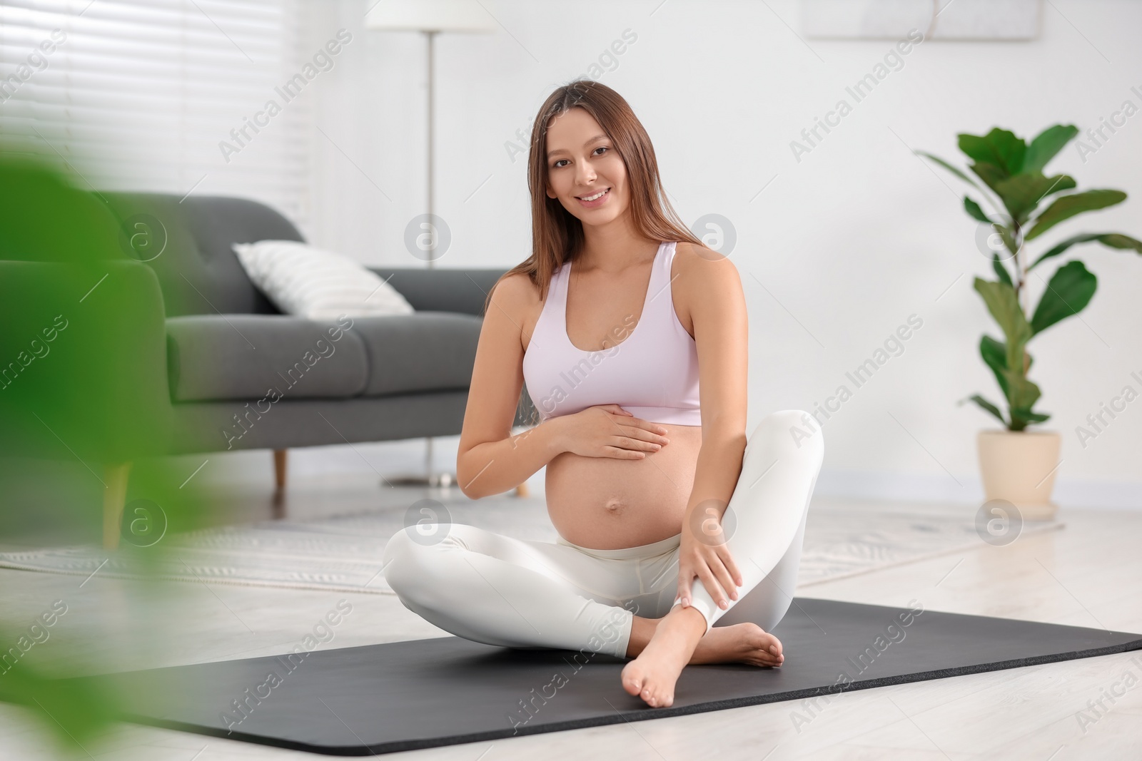 Photo of Pregnant woman sitting on yoga mat at home