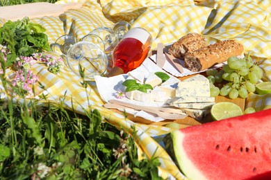 Photo of Picnic blanket with delicious food and wine on green grass outdoors, closeup