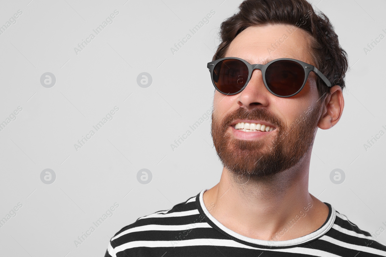 Photo of Portrait of smiling bearded man with stylish sunglasses on light grey background, closeup. Space for text