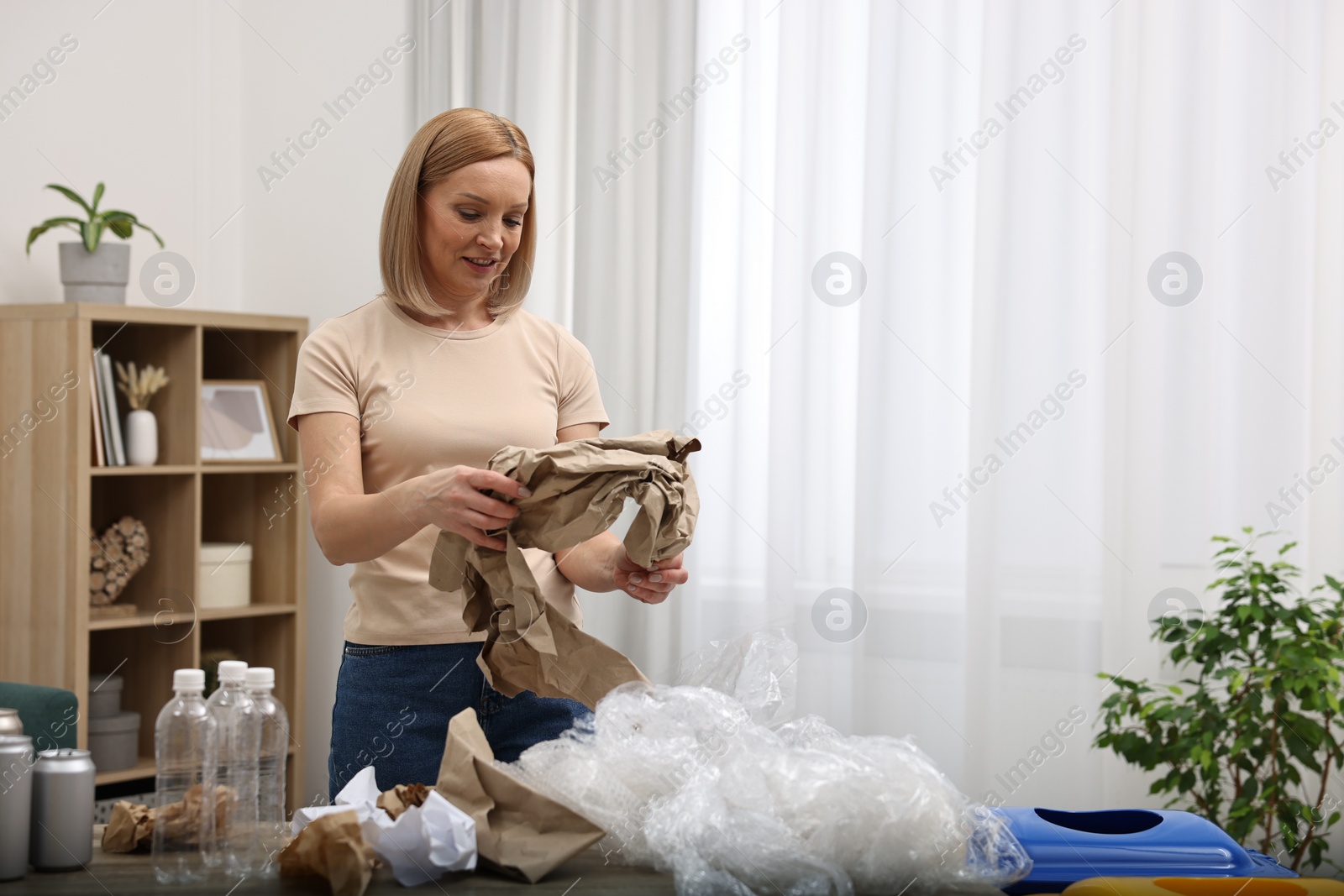 Photo of Smiling woman separating garbage in room. Space for text