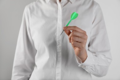 Businesswoman holding green dart on light background, closeup