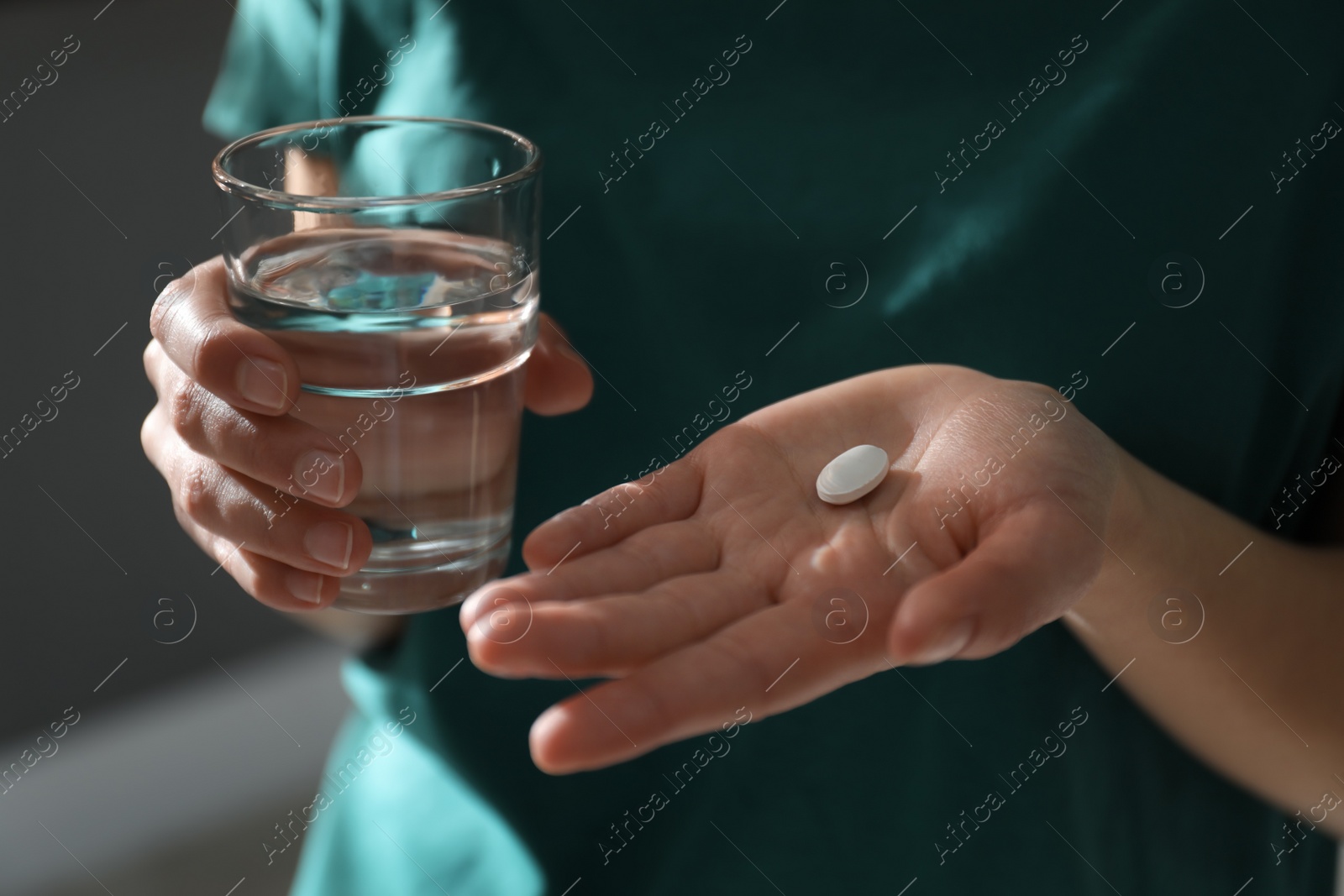 Photo of Young woman with abortion pill and glass of water on blurred background, closeup