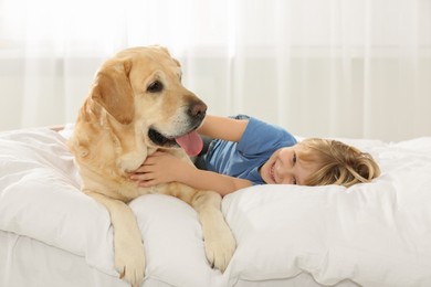 Photo of Cute little child with Golden Retriever on bed at home. Adorable pet