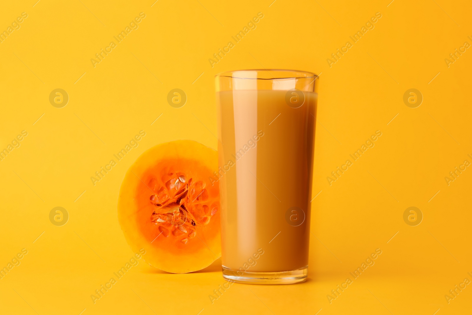 Photo of Tasty pumpkin juice in glass and cut pumpkin on orange background