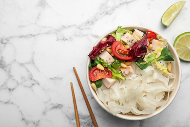 Tasty cooked rice noodles with chicken and vegetables on white marble table, flat lay. Space for text