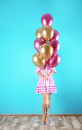 Photo of Young woman hiding behind air balloons near color wall