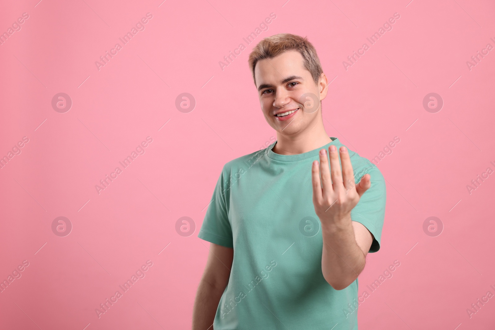 Photo of Happy man inviting to come in against pink background, space for text