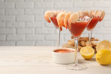 Photo of Tasty shrimp cocktail with sauce in glasses and lemon on light wooden table, space for text