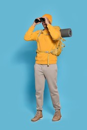 Photo of Happy tourist with backpack looking through binoculars on light blue background