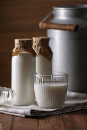 Photo of Tasty fresh milk in can, bottles and glass on wooden table
