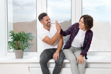 Photo of Happy couple giving high five while sitting on windowsill in new apartment. Moving day