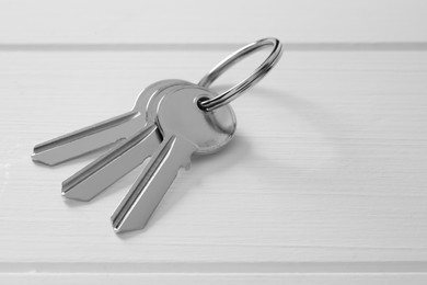 Photo of Keys with ring on white wooden table, closeup. Space for text