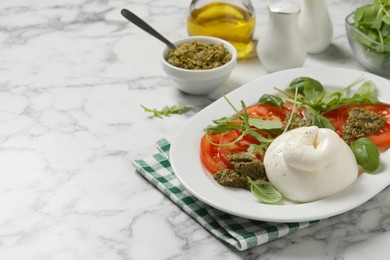 Photo of Delicious burrata salad with tomatoes, arugula and pesto sauce served on white marble table. Space for text