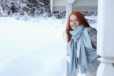Photo of Beautiful young woman looking out from wooden gazebo on snowy day outdoors, space for text. Winter vacation