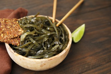 Photo of Tasty seaweed salad in bowl served on wooden table, closeup