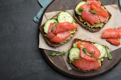 Photo of Tasty bruschettas with salmon, guacamole and microgreens on black table, top view