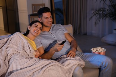 Photo of Couple watching movie with popcorn on sofa at night